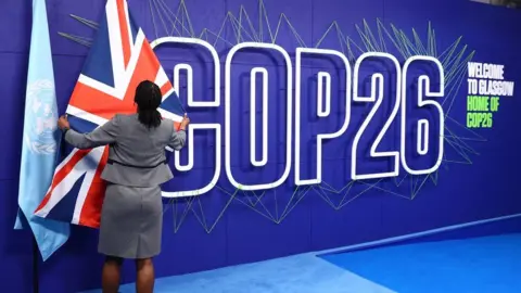 A summit organiser adjusts flags before the arrival of leaders for the COP26 UN Climate Summit in Glasgow on 1 November 2021