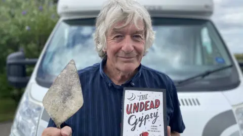 Mr Woodhouse with a tool in one hand and his book in the other