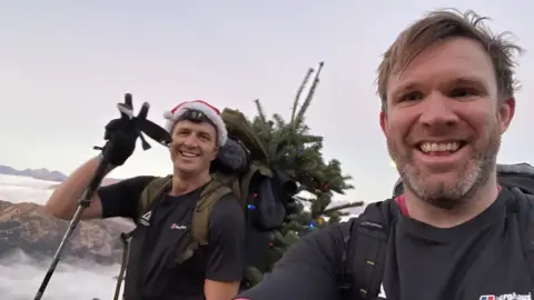 ED JACKSON Ed Jackson and Ross Stirling on their climb. They are both smiling. Ed is wearing a Santa hat.