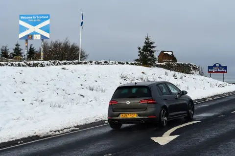 Andy Buchanan / Getty Images Snow blankets the ground by a sign welcoming drivers to Scotland