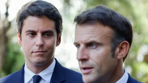 LUDOVIC MARIN/AFP/POOL French Education and Youth Minister Gabriel Attal (L) looks at France's President Emmanuel Macron (R) addressing the audience at the 'lycée professionnel de l'Argensol' or Argensol vocational school during his visit of the school in Orange, Southeastern France on September 1, 2023