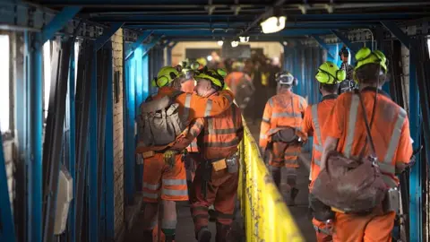OLI SCARFF/AFP/Getty Images group of men in high vis walking to shift in coal mine