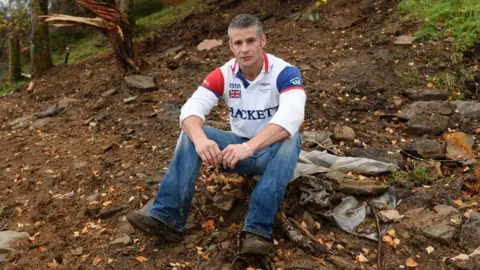 Wales News Service Mike Allen sitting where his cabin once was