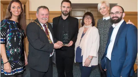DCSDC Johnny McDaid receiving his award from Mayor of Derry Maolíosa McHugh. Also pictured is the musician's mother Pauline, sisters Aine and Síle and brother Rory