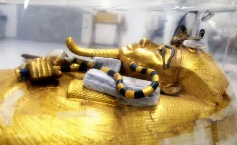 PA Media The golden coffin of Tutankhamun is seen under protective plastic sheets.