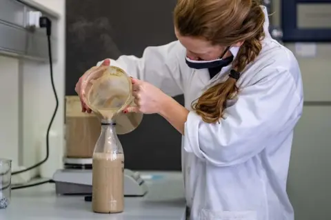 Tommy Trenchard Woman pouring mixture into a bottle