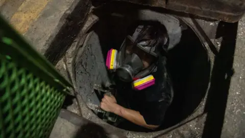 Getty Images An anti-government protester attempts to escape Hong Kong Polytechnic University by going through a sewer on November 19, 2019