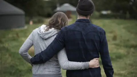 Getty Images Young man and woman walking with their arms around each other on a glampsite while walking towards yurt