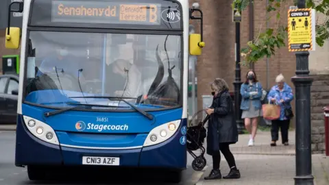 Getty Images Woman boards a bus wearing a face covering