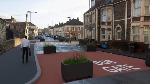 Bristol City Council Concept image of the liveable neighbourhood. It shows a street with houses running down either side. There are four planters placed on each corner of a bus gate. Further up the road, there is a pedestrian crossing. There is a man walking up the pavement towards the crossing.