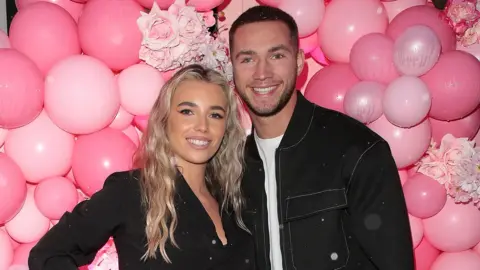 Getty Images Lana Jenkins and Ron Hall, posing in front of pink balloons - they're both wearing black outfits and smiling.