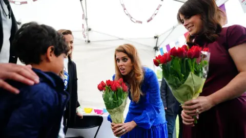 PA Media Princess Beatrice (centre) and Princess Eugenie are presented with flowers as they arrive at the Big Jubilee Lunch in Paddington