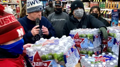 Reuters Shoppers crowd a display of bottled water at a supermarket in Abilene, Texas, 15 February 2021