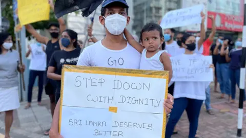 A man holds his baby and a protest sign reading: "Step down with dignity. Sri Lanka deserves better"