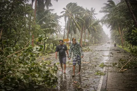 Alren Beronio / AFP Two people walk along a road past uprooted trees