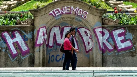 AFP A couple walks by graffiti reading "We Are Hungry" in Caracas on August 8, 2017.