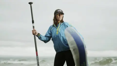  Brett Harkness Sian Sykes with a paddleboard stood in the sea