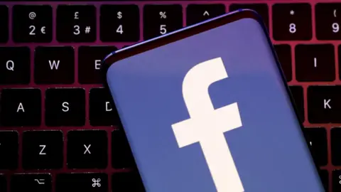 A phone with the facebook logo on it on a computer keyboard