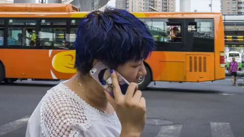 AFP Woman talking into a mobile phone while crossing the road