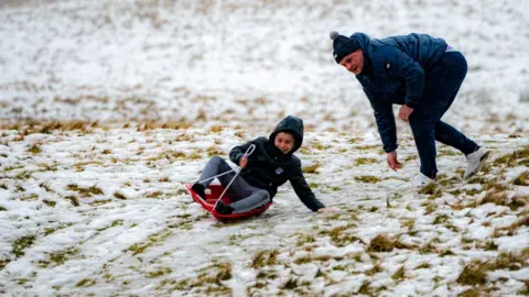 PA Media A sledger makes the most of the snow on an icy and snowy hill as rain falls in the Brecon Beacons National Park, Wales. Snow and ice have swept across parts of the UK,