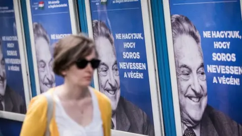 Alamy A woman walks past a wall of Soros posters