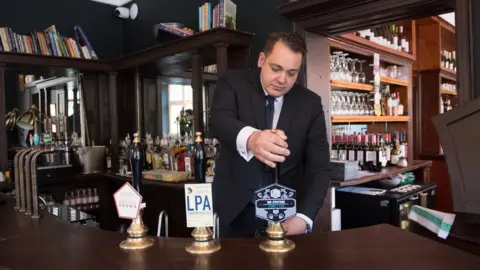 PA Media Man pulls a pint of beer behind the bar