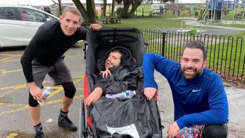 Ed Harris Three people smiling at a camera, one in an accessible chair