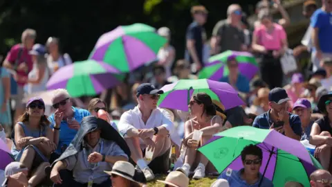 PA Media Spectators shield from the sun on day twelve of the 2022 Wimbledon Championships