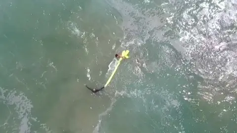 NSW government A screengrab shows the two boys clinging to the yellow inflatable as they swim back to shore