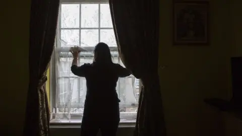 Andrew Aitchison/Getty Images An unidentified lady stands silhouetted in front of her living room window