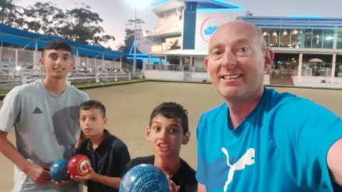 Family photo Dave with his sons Jake, Thomas, and Dylan. All three are holding bowls while on holiday in Australia.