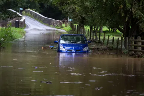 Shutterstock A stranded car in flood water in Merthyr Mawr