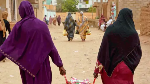 AFP Women walk down a street carrying bags in Greater Khartoum, Sudan - May 2023