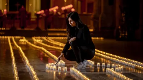 PA Media Holly Wilson, whose grandmother Ada Wilson passed away during the pandemic, lights a candle in Belfast Cathedral - the floor of the cathedral is covered in the lights