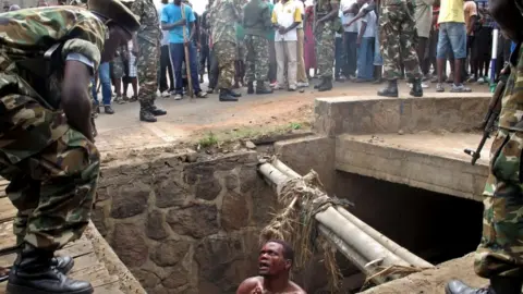AFP A bloodied man in a pit begs as he is surrounded by soldiers