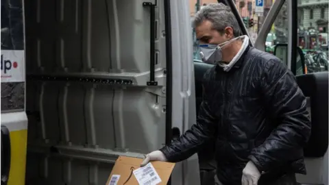 Getty Images A courier, wearing a respiratory mask, handles an Amazon parcel