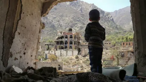 Getty Images A Yemeni child looking out at buildings that were damaged in an air strike in the southern Yemeni city of Taez.
