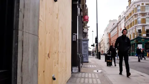 Getty Images A man walks past a boarded-up shop on Mortimer Street in London, England, 2019.