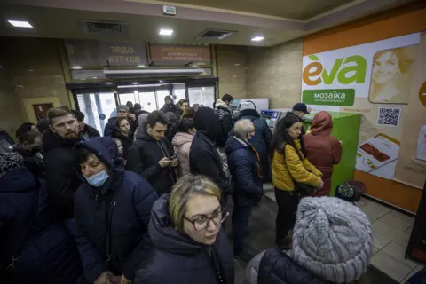 Anadolu Agency via Getty Images People line up to withdraw money from ATMs after Russia's military operation on 24 February 2022, in Kramatorsk