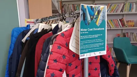 Cambridgeshire County Council Child and adult coats on a rack at Bar Hill library.