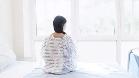 Getty Images Woman in hospital gown on bed