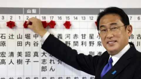 EPA Japanese Prime Minister Fumio Kishida puts rosettes by LDP successful election candidates' names on a board at the party headquarters in Tokyo. Photo: 31 October 2021