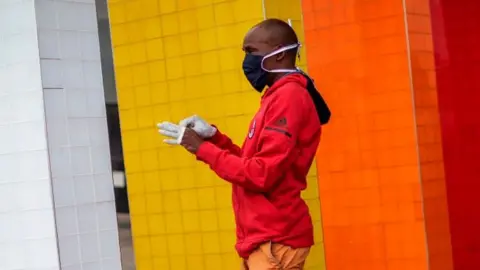 AFP A man wearing a face mask puts on a pair of gloves at the entrance of a shopping mall in Alexandra, Johannesburg, in 2020.
