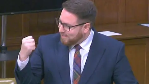 PARLIAMENT Man with beard and glasses shaking a fist and smiling