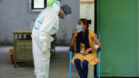 Getty Images A health worker in PPE talking to a woman during a swab Covid-19 rapid antigen tests at a government school.