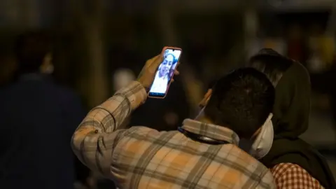 Getty Images An Iranian couple video call to congrats the beginning of the New Year to their relatives as they stand in the Water and Fire Park in northern Tehran on March 20, 2022.