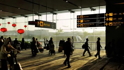 Getty Images Passengers with bags and trolleys walking under signs for gates in Terminal 3 Heathrow