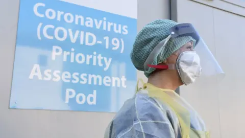 PA Media A nurse in protective clothing, face mask and visor at a coronavirus assessment unit in Antrim