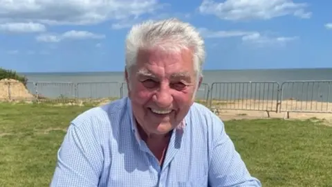 Jonah Fisher Portrait of man sitting with sea in background.