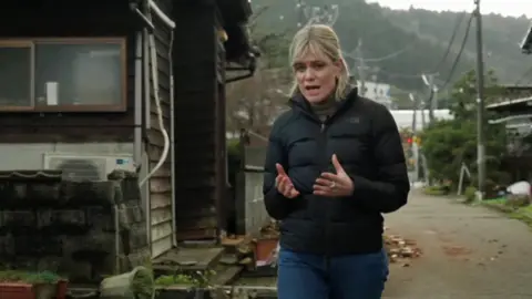 Jean MacKenzie walks along road with damaged buildings on either side